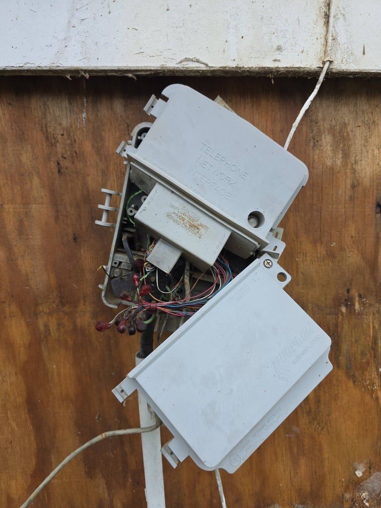 Weathered electrical junction boxes mounted on a wooden wall with exposed wiring and connections